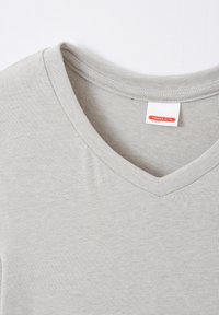 T-shirt grigia a V in tessuto morbido. Presenta un colletto a coste e un'etichetta con la scritta "THERMOLACTYL by Damart". Tessuto dalla texture liscia.