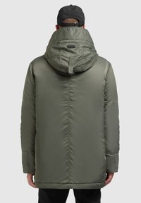 Olivengrøn pufferjakke med hætte, der har lynlås lukning, quiltet mønster og elastiske manchetter. Glat tekstur og mellemlang design.
