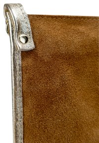 Dettaglio di una borsa in suede marrone con una tracolla metallica argentata. Presenta una finitura testurizzata, accenti di hardware lisci e cuciture a contrasto.