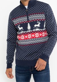 Marineblauer Strickpullover mit Halb-Reißverschluss, versehen mit einem Weihnachtsmuster aus Rentieren, Bäumen und geometrischen Designs in Rot und Weiß.