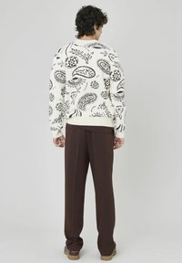 Pull en tricot blanc avec des motifs cachemire et floraux marron, associé à un pantalon marron. Détails des bordures côtelées visibles aux poignets et à l'ourlet.