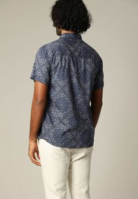 Korte mouwen, marineblauw patroon overhemd met een bloemenontwerp en een button-down kraag, gedragen met lichtgekleurde broek.