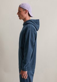 Navyblauwe hoodie van zacht materiaal, met een kangoeroezak, verstelbare capuchon en geribde manchetten. Gecombineerd met bijpassende broek.