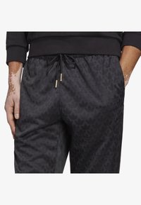 Mustat juoksuhousut, joissa on teksturoitu lehtikuvio, joustava vyötärö, jossa on kiristysnyöri, sekä kontrastiväriset kultaiset yksityiskohdat.