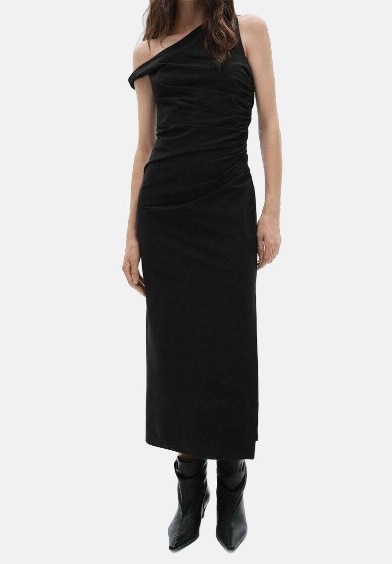 Vestido negro de un solo hombro hecho de tejido suave, con detalles fruncidos y una silueta ajustada, combinado con botines negros hasta el tobillo.