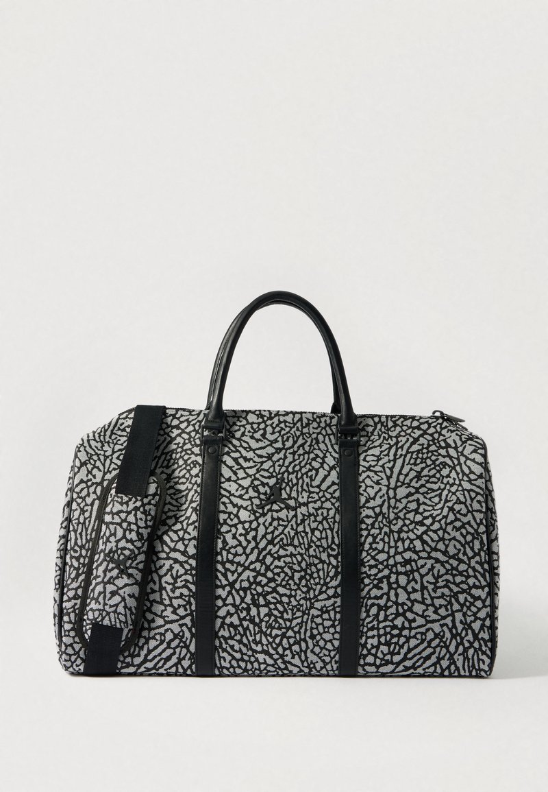 Saco de viagem de padrão preto e cinza com alças e tiras em couro preto, apresentando uma forma arredondada e fecho de zíper. Tecido texturizado.