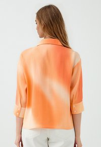 Orangeshirt mit Farbverlauf aus leichtem Stoff, mit Kragen und hochgerollten Ärmeln. Glatte Textur mit sanfter Farbänderung.