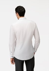 Camicia bianca a maniche lunghe con una texture liscia, colletto classico e polsini abbottonati. Presenta una leggera lucentezza e una vestibilità sartoriale.