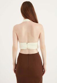 Witte haltertop met een ritssluiting aan de achterkant, gecombineerd met een nauwsluitende bruine rok met een achternaad en ritsdetail.