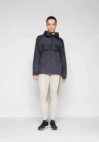 Pull-over à quart de zip en marine foncé et noir avec des manches longues, doté d'une capuche ajustable et de poignets élastiques. Associé à des leggings beige clair.