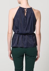 Marinblå halterneck-topp med en rynkad midja och knytning bak; tillverkad av lätt tyg med en mjuk yta.