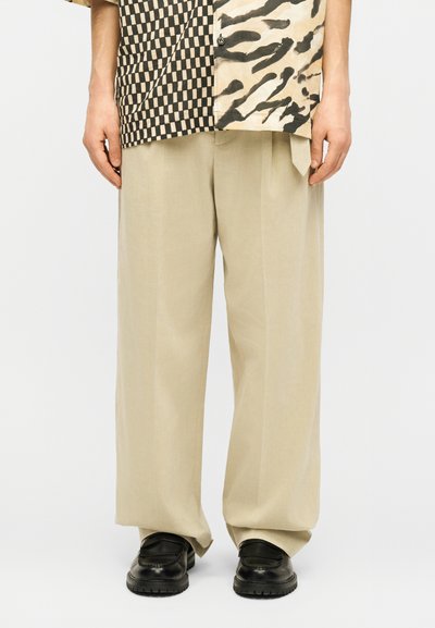 Μπεζ παντελόνια φαρδιάς γραμμής συνδυασμένα με μαύρα chunky loafers και πουκάμισο με μοτίβα σκακιέρας και ζωικών εκτυπώσεων σε μαύρο και λευκό.