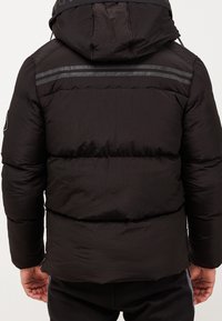 Schwarze Pufferjacke mit Kapuze, mit gesteppten Abschnitten, reflektierenden Streifen an den Schultern und einer strukturierten Außenseite.