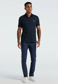 Dunkelblaues Poloshirt mit geometrischem Muster, kurzen Ärmeln und Kragen. Kombiniert mit dunkelblauen Hose und weißen Turnschuhen.