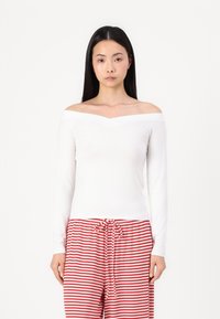Long-sleeve off-the-shoulder white top with a smooth texture, paired with red and white striped pajama pants featuring a drawstring waist.