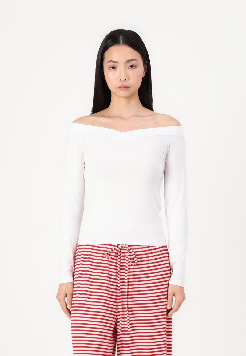 Long-sleeve off-the-shoulder white top with a smooth texture, paired with red and white striped pajama pants featuring a drawstring waist.