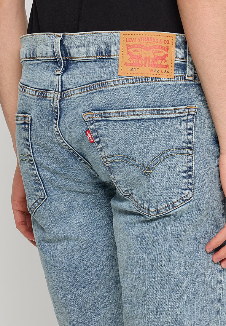 Vaqueros de mezclilla azul claro con corte ajustado, que cuentan con bolsillos traseros y una etiqueta de piel marrón con texto rojo en la cinturilla.