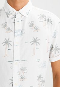Kurzärmeliges, knöpfbares Hemd aus weißem Stoff mit Palmen- und Wellenmustern in Pastellfarben. Leichtes, lässiges Design.