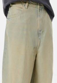 Jeans in denim verde chiaro con una vestibilità comoda, dotati di cinque tasche e una leggera scoloritura. Dettagli cuciti in blu, senza hardware visibile.