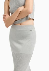 Crop top a coste grigio chiaro abbinato a una gonna. Presenta una texture liscia con un leggero lucido, vita elasticizzata e un piccolo dettaglio con logo.