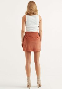 En ribbad vit linne-top förslags med en plommonfärgad manchestermini-kjol. Kjolen har framfickor och rak skärning. Beiga åtsittande högklackade stövlar.