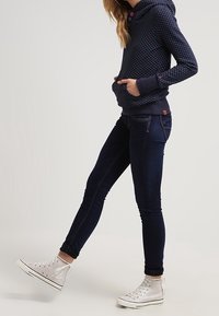 Marinblå hoodie med prickar, framficka och snörning, i kombination med mörka skinny jeans och silverfärgade hög-top sneakers.