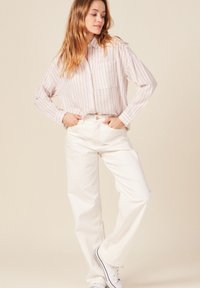 Camicia button-up a righe rosa chiaro e bianca, vestibilità rilassata, abbinata a pantaloni bianchi a vita alta, entrambi in tessuto morbido con uno stile casual.
