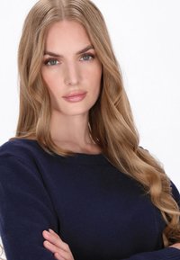 Sötét tengerészkék pulóver, kerek nyakkivágással és hosszú ujjakkal. Simább textúra, a modellen hosszú, hullámos haj van, amely a vállára omlik.