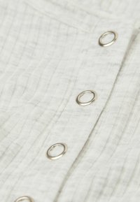 Vitt texturerat tyg med vertikala linjer, som har silverfärgade metallknapphål. Mjukt, lätt material med subtila färgvariationer.