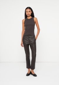 Top bej cu mânecă scurtă, cu un design mulat, combinat cu pantaloni slim-fit din piele ecologică maro închis, având o închidere frontală cu buton.