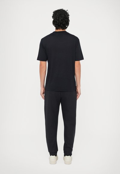 Fekete, rövid ujjú póló kerek nyakkivágással, fekete texturált nadrággal és világos színű tornacipővel, hátulnézetben.