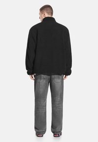Czarna polarowa kurtka z wysokim kołnierzem, noszona na szare dżinsowe spodnie. Materiał wydaje się miękki i teksturowany, z luźno dopasowanymi rękawami.