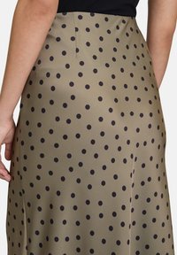 Jupe vert olive à pois noirs, fabriquée en tissu lisse. Présente une taille ajustée et possède un éclat subtil.