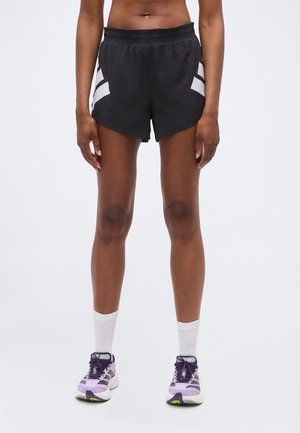 Person wearing black athletic shorts with white side panels, white crew socks, and purple running shoes, standing on a plain white background.