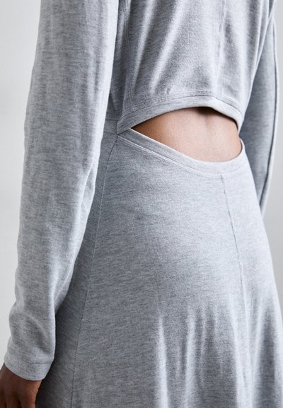 Grijze twee-delige outfit bestaande uit een top met lange mouwen en een uitsnede op de rug, en een bijpassende onderkant, beide in een zachte, gestructureerde stof.