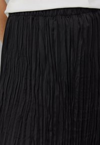 Jupe plissée noire avec une taille élastique, présentant une texture lisse et des plis verticaux pour un mouvement et un flux améliorés.