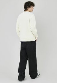 Pull en tricot crème avec une texture côtelée, associé à un jean noir à coupe ample et des baskets. Le pull a un col rond et une coupe décontractée.