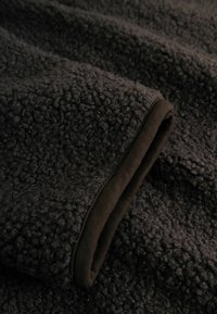 Tessuto in pile grigio scuro con una superficie texturizzata e soffice e un bordo brunito a contrasto lungo il bordo. Aspetto morbido e caldo.