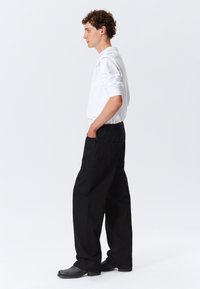 Sorte bukser med vide ben og tekstureret finish, stylet med en tætsiddende hvid langærmet skjorte. Bukserne har sidelommer og et diskret design.