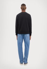 Svart genser med rund hals og ribbethammer, kombinert med lys blå straight-leg jeans, med baklommer og en avslappet passform.