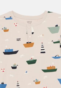 Βιολογικό βαμβακερό t-shirt σε μπεζ χρώμα με ναυτι κό σχέδιο που περιλαμβάνει πολύχρωμα πλοία, σύννεφα, έναν φάρο και ένα σωσίβιο. Λαιμόκοψη με δύο κουμπιά.