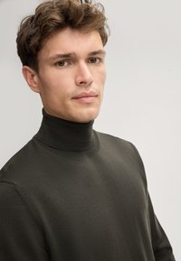 Dunkelgrüner Rollkragenpullover mit strukturiertem, geripptem Strick. Mit hohem Kragen und enganliegender Silhouette, die sanfte Linien betont.