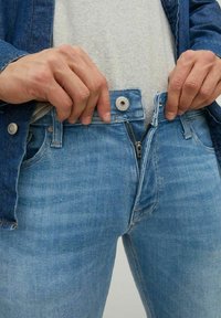 Jeans de mezclilla azul claro con cierre de cremallera y botón en la cintura, que presentan un diseño de corte recto y detalles de costura visibles.