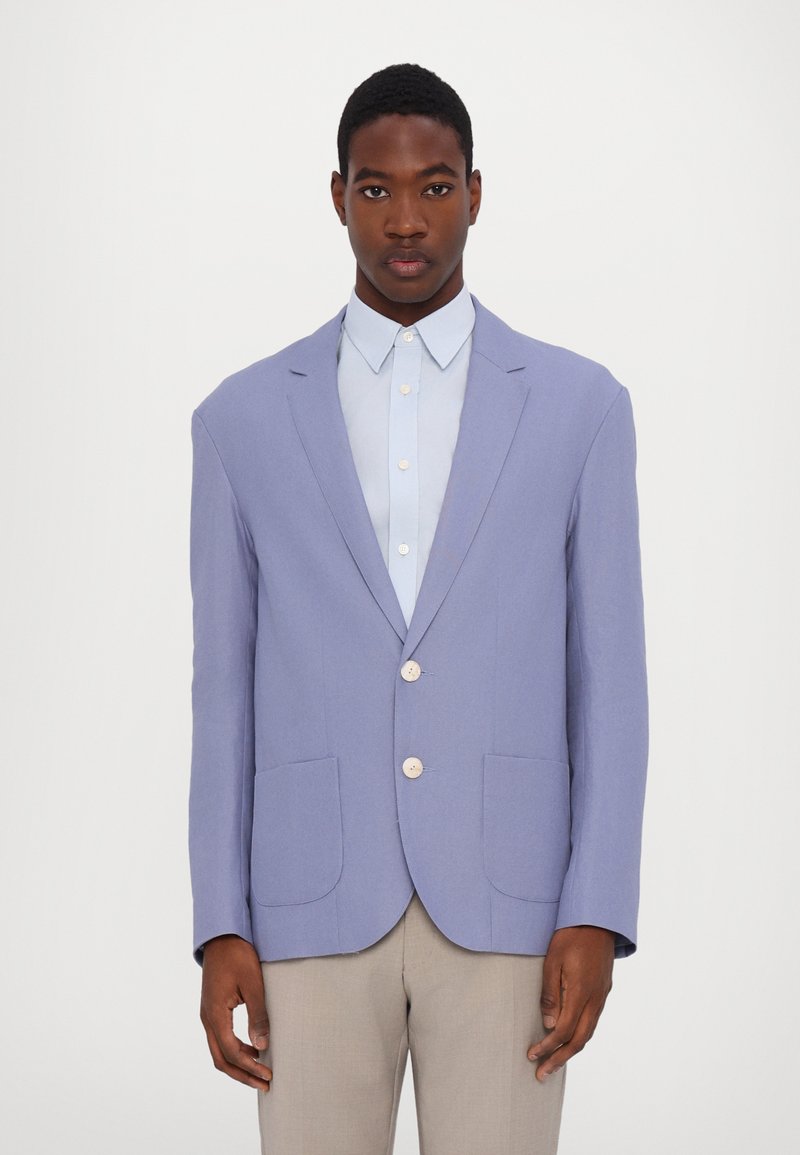 Light purple blazer with two front pockets, single-button closure, and notched lapels. Worn over a light blue collared shirt.