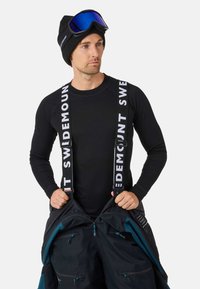 Zwart thermisch shirt met lange mouwen, zwarte skibroek met witte banden met de opdruk "SWIDEMOUNT," en blauw-getinte skibril.