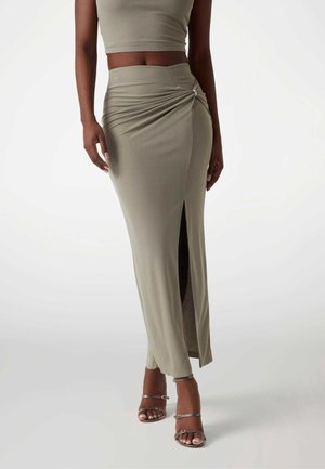 Femme portant une tenue deux pièces vert olive avec une jupe froncée taille haute avec une fente devant et des sandales à talons hauts à brides.