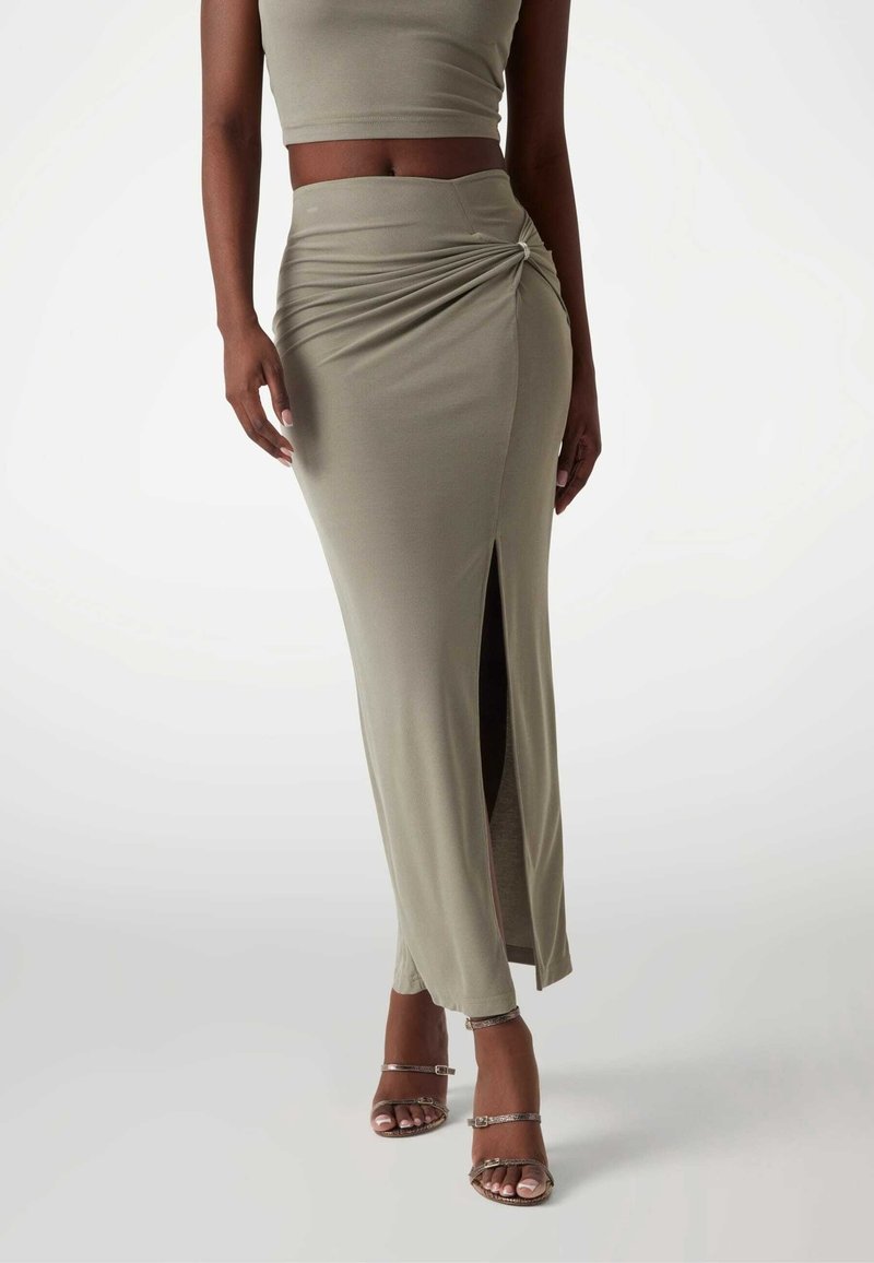 Femme portant une tenue deux pièces vert olive avec une jupe froncée taille haute avec une fente devant et des sandales à talons hauts à brides.