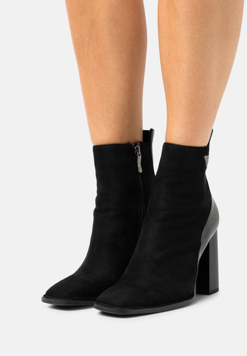 Bottines noires en daim avec fermeture éclair, présentant un bout pointu et un talon épais, mettant en valeur un accent en cuir lisse.