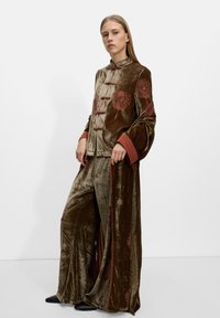 Aksamitny strój w zielonkawo-brązowym kolorze z czerwoną haftą kwiatową, w tradycyjnym stylu, z zapięciem na guziki i szerokimi rękawami.