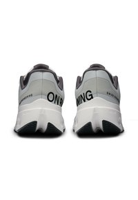 Chaussures de sport grises et blanches avec une tige texturée, une marque visible sur les côtés et une semelle à design rembourré.